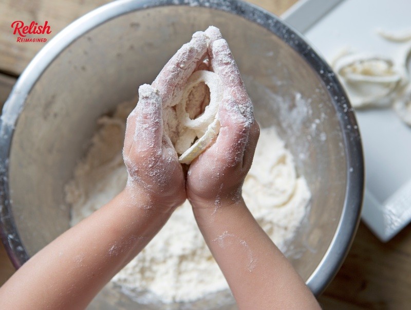 A child's flour-covered hands cupped over a mixing bowl, with the Relish Reimagined logo in the corner.